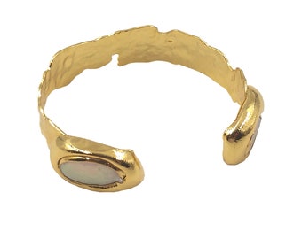 May include: Gold-toned cuff bracelet with a textured, organic design. The open-ended bracelet features an oval-shaped, iridescent stone on each end. The cuff has a hammered appearance, adding to its unique, handcrafted aesthetic. A stylish piece of jewelry.