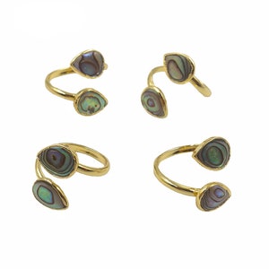 May include: Four gold rings each featuring two teardrop-shaped abalone shell inlays. The rings are open and adjustable.