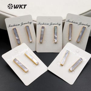 May include: Five pairs of gold earrings with white rectangular shell-shaped stones. Each pair is displayed on a white card with the text "Fashion Jewelry".