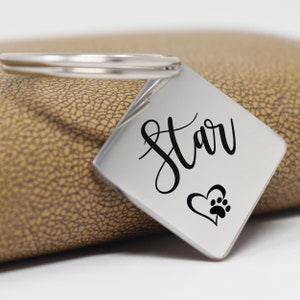 May include: Silver keychain with a square tag that says "Star" in cursive with a paw print inside a heart.