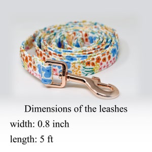 May include: A white dog leash with a floral pattern in shades of blue, orange, and pink. The leash is 5 feet long and 0.8 inches wide. It has a rose gold metal clasp.