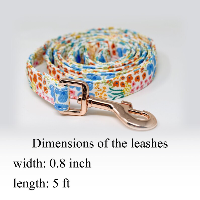 May include: A white dog leash with a floral pattern in shades of blue, orange, and pink. The leash is 5 feet long and 0.8 inches wide. It has a rose gold metal clasp.