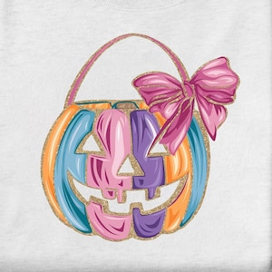 May include: A white t-shirt with a colorful pumpkin design. The pumpkin is shaped like a trick-or-treat bag with a pink bow on top. The pumpkin is decorated with orange, blue, pink, and purple stripes.