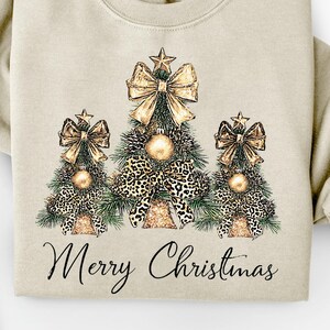 Könnte beinhalten: Beiges Sweatshirt mit drei Weihnachtsbaum-Designs mit goldenen Schleifen, Leopardenmuster-Akzenten und Stern-Toppern. Der Schriftzug "Merry Christmas" ist darunter aufgedruckt. Ein festliches Kleidungsstück für die Feiertage.