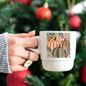 Pu&ograve; includere: Tazza in ceramica bianca con un design autunnale con tre zucche con accenti floreali. Le zucche sono arancioni, marroni e verdi con un motivo leopardato.