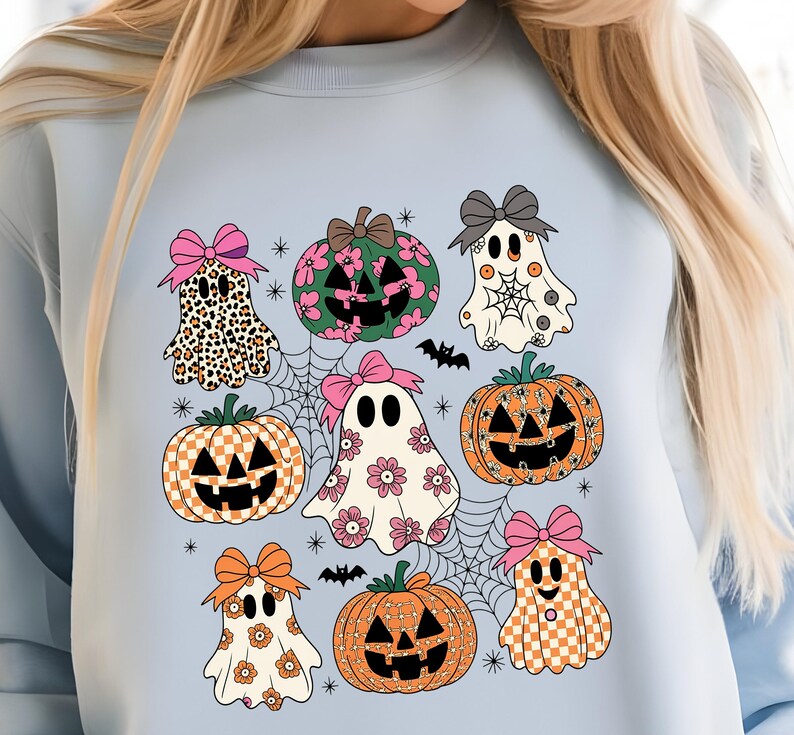 May include: Light blue sweatshirt featuring a Halloween-themed design. The design includes cartoon ghosts, pumpkins, spiderwebs, and bats. The ghosts have various patterns, including leopard print, floral, and checkered. The pumpkins have carved faces.