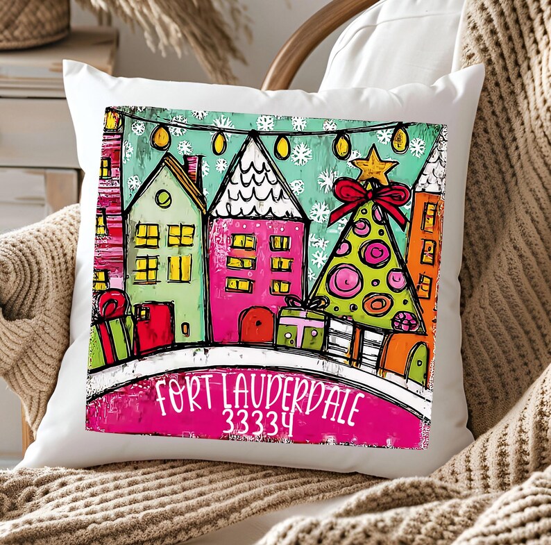 May include: White square throw pillow with a colorful illustration of houses, a Christmas tree, and gifts. The text "FORT LAUDERDALE 33334" is printed on the pillow. The design features a festive holiday theme.