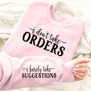 May include: Pink sweatshirt with the text "i don't take ORDERS" on the front and "i barely take SUGGESTIONS" on the sleeve.
