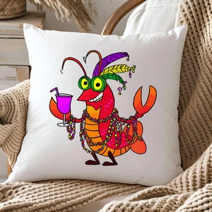 May include: White square throw pillow featuring a cartoon crawfish with a cocktail. The crawfish is red, orange, and yellow, wearing Mardi Gras beads and a feathered headdress. It holds a purple drink with a straw.