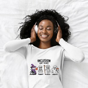 May include: White long-sleeve t-shirt with a graphic of Halloween characters in wheelchairs, a skeleton, a mummy, and a ghost. The text "Inclusion Isn't Scary" is printed on the shirt.