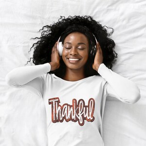 K&ouml;nnte beinhalten: Ein wei&szlig;es Langarmshirt mit dem Wort "Thankful" in brauner und wei&szlig;er, abgenutzter Schrift.