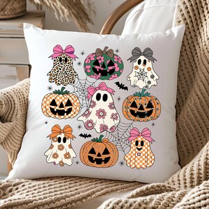 May include: White square pillow featuring a Halloween-themed design. The design includes cartoon ghosts, pumpkins, spiderwebs, and bats. The ghosts and pumpkins are decorated with patterns and bows in various colors, including pink, orange, and black. The pillow is on a neutral-toned surface.
