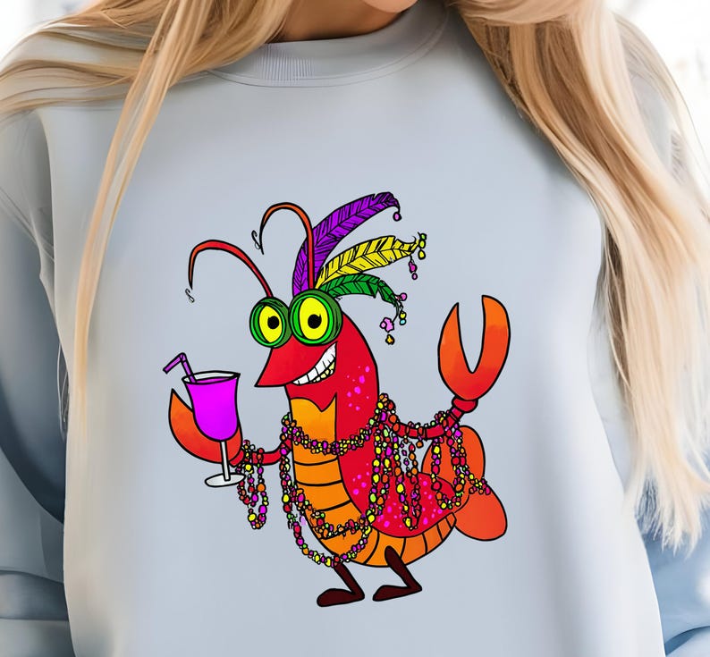 May include: Light blue sweatshirt featuring a cartoon crawfish with a festive Mardi Gras design. The crawfish is red, orange, and yellow, wearing a feathered headdress, beads, and holding a cocktail. The design is a fun, colorful illustration.