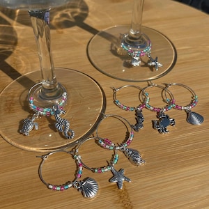 May include: Set of six colorful glass charms with sea-themed charms, including a starfish, seashell, crab, seahorse, and turtle. The charms are attached to silver rings.