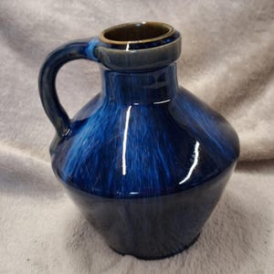 May include: A blue ceramic pitcher with a handle. The pitcher has a glossy finish with dark blue and light blue streaks. The rim and handle are a darker shade of blue. The pitcher is a decorative item.