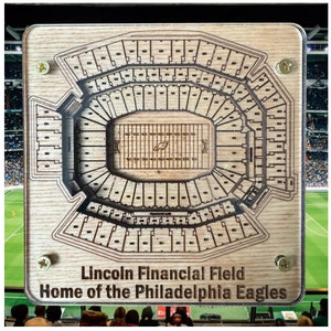 May include: A wooden sign with a laser-cut design of Lincoln Financial Field, home of the Philadelphia Eagles. The sign has a brown wood background and black lines outlining the stadium seating.