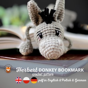 Könnte beinhalten: Gehäkelter Esel-Lesezeichen in Grau mit schwarzen Akzenten. Der Esel hat einen traurigen Gesichtsausdruck und liegt auf einem Buch. Der Text "Herbert Donkey Bookmark crochet pattern" ist sichtbar.