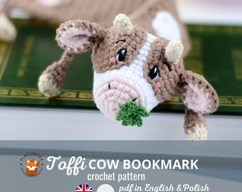 May include: A crocheted cow bookmark with brown and white fur, holding a green leaf in its mouth. The bookmark is lying on a book with a green cover. The text "Toffee COW BOOKMARK crochet pattern pdf in English & Polish" is below the image.