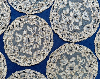 Könnte beinhalten: Eine Sammlung cremefarbener, kreisförmiger Spitzendeckchen mit floralen Mustern. Die Deckchen sind auf einer blauen Oberfläche angeordnet und zeigen ihr filigranes Lochmuster. Jedes Deckchen weist aufwendige Details auf und erzeugt eine elegante, Vintage-Ästhetik.