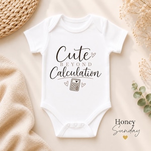 May include: A white short-sleeved baby bodysuit featuring the text "Cute BEYOND Calculation" in dark brown script and block lettering. Below the text is a small graphic of a calculator with a heart on its screen, flanked by two small hearts.
