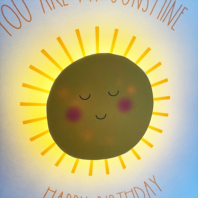 May include: A yellow sun with a smiling face and closed eyes. The sun has a light yellow glow around it. The text "You are my sunshine" is written above the sun and "Happy Birthday" is written below the sun.