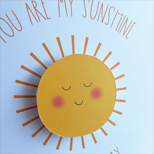 May include: A yellow sun with a smiling face and closed eyes. The sun has rosy cheeks and is surrounded by orange rays.