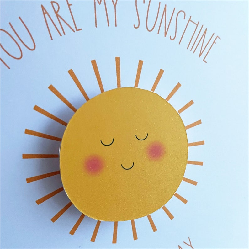 May include: A yellow sun with a smiling face and closed eyes. The sun has rosy cheeks and is surrounded by orange rays.