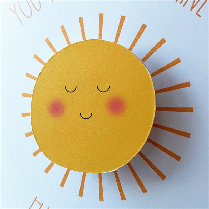 May include: A yellow sun with a smiling face and closed eyes. The sun has a red blush on each cheek. The sun is surrounded by orange rays.