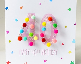 May include: A pink birthday card with the number 40 made of colorful pom-poms on a silver wire. The card has a white background with pink hearts and stars. The text "Happy 40th Birthday" is printed on the card.