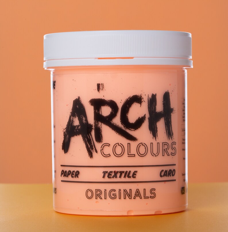 May include: A peach-colored jar of paint with a white lid. The jar is labeled "ARCH COLOURS" in black lettering. The label also says "PAPER, TEXTILE, CARD" and "ORIGINALS".