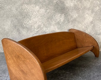 May include: A wooden bench with curved arms and a simple design. The bench is made of light brown wood and has a natural finish.