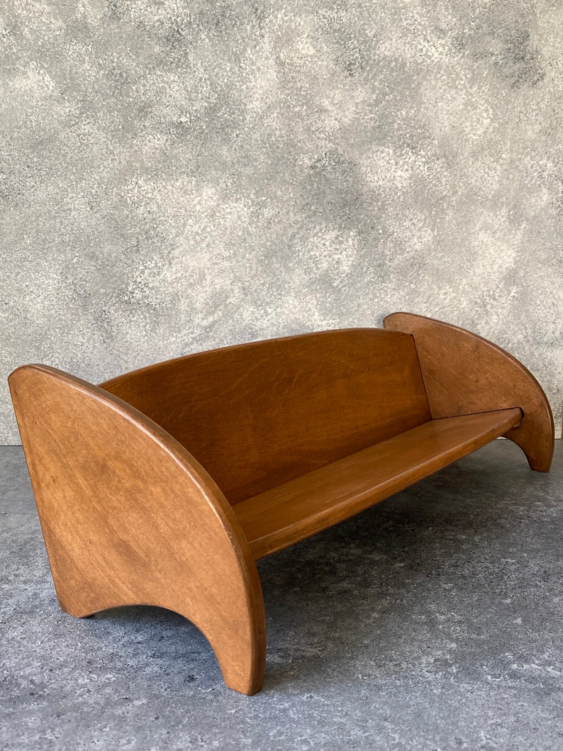 May include: A wooden bench with curved armrests and a natural wood finish. The bench is made of solid wood and has a simple, elegant design.