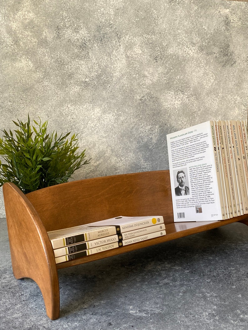 May include: A wooden bookshelf with three books on it. The books are titled "Marcus Aurelius", "Victor Hugo", and "L.N. Tolstoy". The bookshelf is sitting on a gray surface.