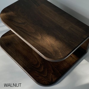 May include: A two-tiered wooden shelf with rounded edges, finished in a dark walnut stain. The shelf is mounted to a wall.