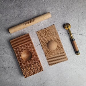 Könnte beinhalten: Ein Satz aus vier Holzwerkzeugen zum Erstellen von dekorativen Mustern in Teig. Die Werkzeuge umfassen einen Nudelholz, eine Teigpresse mit einem kreisförmigen Design, eine Teigpresse mit einem geometrischen Design und einen Teigschneider mit einem dekorativen Rad.