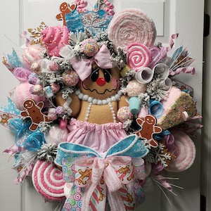 May include: A pink and blue gingerbread girl Christmas wreath with a bow, candy canes, lollipops, and gingerbread cookies.