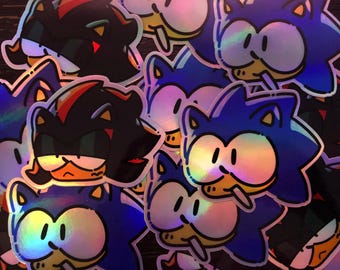 May include: A collection of holographic stickers featuring cartoon characters. The stickers showcase two distinct characters: a blue hedgehog and a black hedgehog with red accents. The stickers have a glossy finish and are scattered across the image.