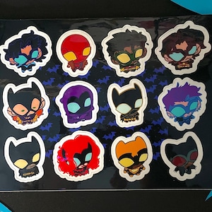 Pode incluir: Uma folha de autocolantes com doze autocolantes individuais recortados de personagens de desenhos animados estilizados com várias cores de cabelo, máscaras e fatos, incluindo desenhos pretos, vermelhos, roxos e cor de laranja.