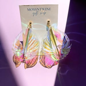 Puede incluir: Un par de pendientes iridiscentes con un acento dorado. Los pendientes tienen forma de abanico y un dise&ntilde;o delicado y femenino. Los pendientes se muestran en una tarjeta blanca con el texto "Mossntwine gift shop".