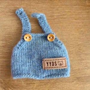 May include: Blue knitted baby overalls with brown buttons and a brown leather patch with the text "YYDS" and a bear icon.