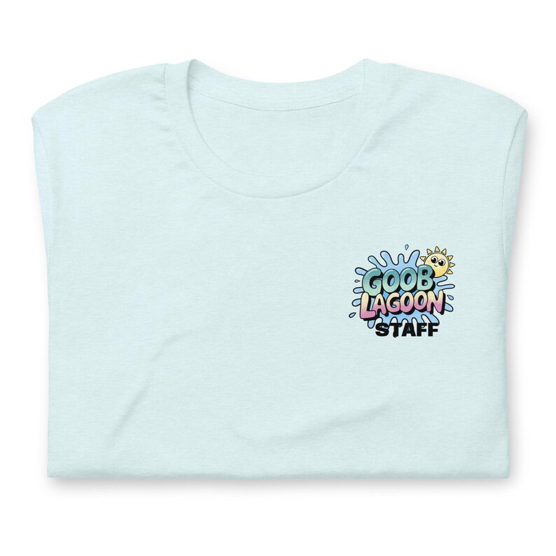 Op de afbeelding: Lichtblauw T-shirt met een ronde hals. De voorkant van het shirt heeft een kleurrijke afbeelding met de tekst "GOOB LAGOON STAFF", vergezeld van een cartoon zon en een waterspetter ontwerp.