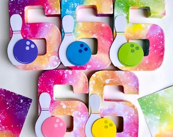 May include: Colorful number six cutouts with bowling pin and ball designs. Each number is painted with a tie-dye pattern in shades of pink, purple, yellow, and green. The bowling balls are blue, green, pink, and yellow.