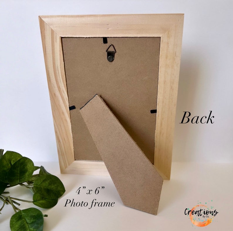 Pu&ograve; includere: Vista posteriore di una cornice in legno chiaro. La cornice misura 10 cm x 15 cm e ha un retro in cartone e un cavalletto. Il testo "Back" &egrave; visibile sulla cornice, insieme al testo "4" x 6" Photo frame".