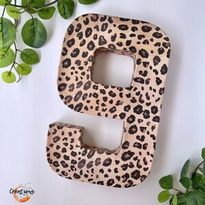 May include: A large, freestanding number nine in a leopard print pattern. The number is made of a light brown material with dark brown spots. The number is surrounded by green leaves and a white background.