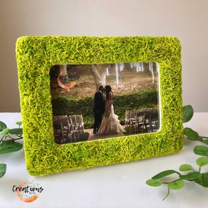 Pu&ograve; includere: Una cornice rettangolare con una vibrante texture verde simile al muschio. La cornice contiene una fotografia di matrimonio di una coppia che si bacia. La cornice ha il testo "Creations by Liz" in basso a sinistra.