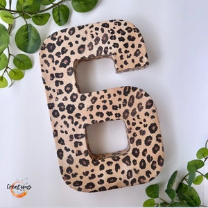 May include: A large, freestanding number six, decorated with a leopard print pattern in shades of tan, brown, and black. The number is made of a thick material and has a hollowed-out center. The word "Creations" is in the lower left corner.