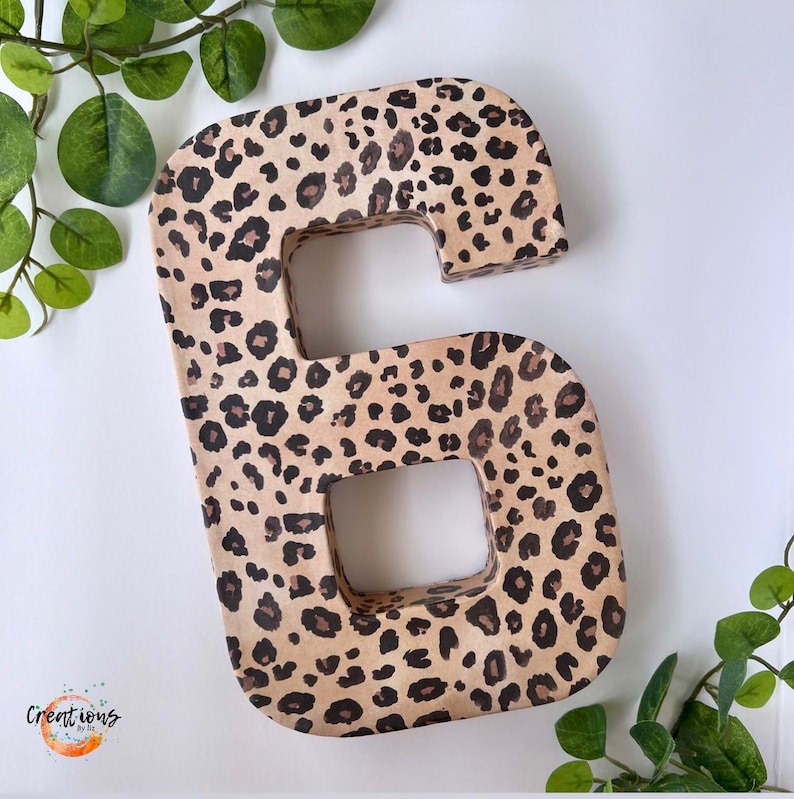 May include: A large, freestanding number six, decorated with a leopard print pattern in shades of tan, brown, and black. The number is made of a thick material and has a hollowed-out center. The word "Creations" is in the lower left corner.