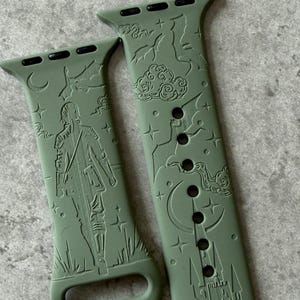 May include: Two green silicone Apple Watch bands with an engraved design. One band features a moon and stars, the other features a figure standing in a field.