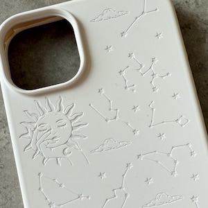 Op de afbeelding: Witte telefoonhoes met een ontwerp van sterrenbeelden, sterren, wolken, een zon en een maan.