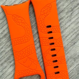 Puede incluir: Un par de correas de reloj de silicona naranja brillante con un diseño de serpiente. Las correas están diseñadas para un reloj inteligente.